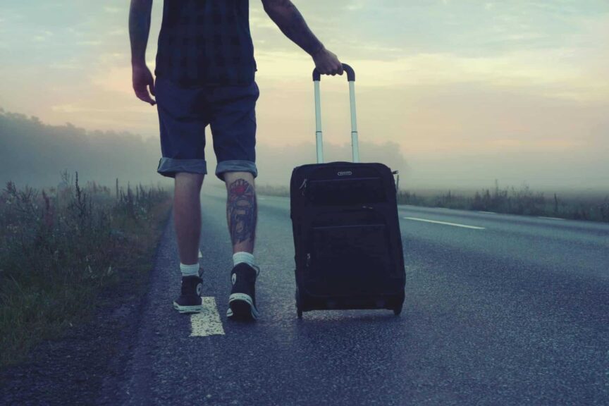 rolling suitcase ban, europe, Man walking with a suitcase along a foggy road at sunrise, symbolizing adventure and travel.