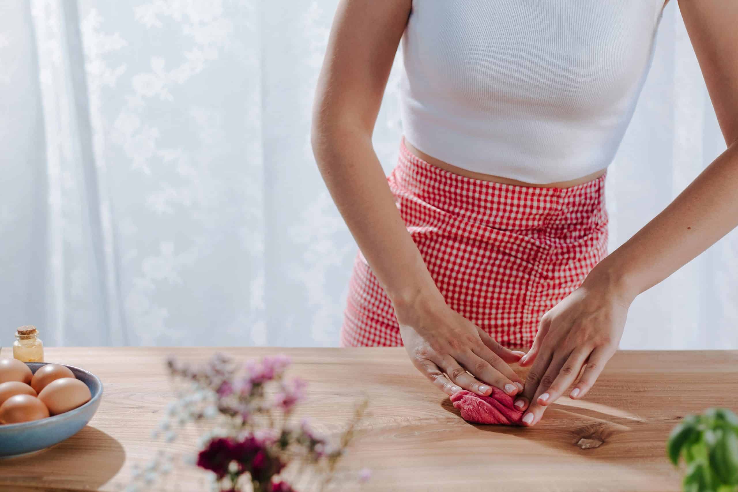 Hands kneading red pasta dough on a wooden board indoors, capturing an intimate cooking moment.