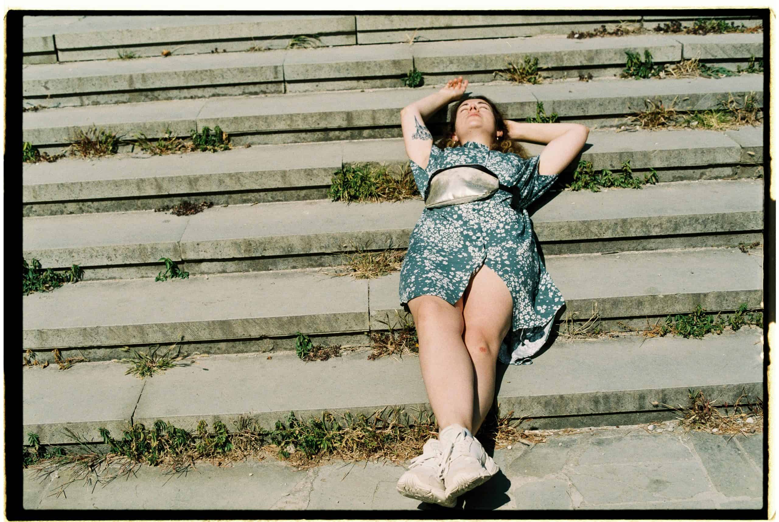 A woman enjoys a sunny day lying on concrete steps, embracing relaxation outdoors.