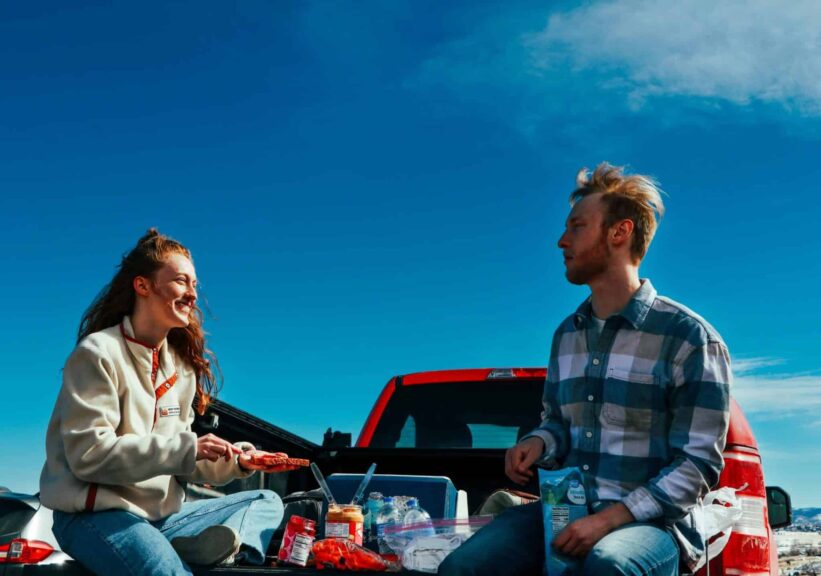 A cheerful couple having a picnic on a truck tailgate under clear blue skies. game day