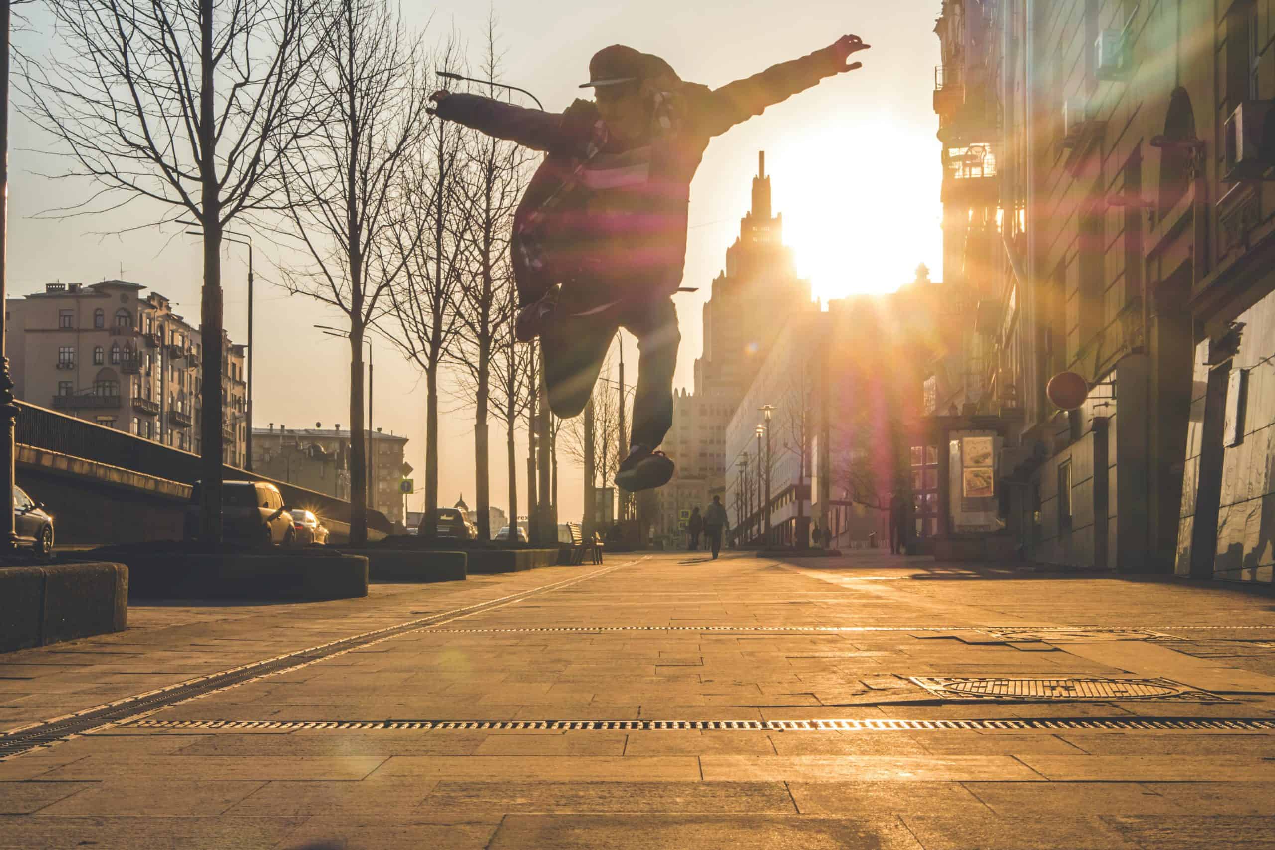 Silhouette of a man jumping energetically in a sunlit urban street at sunset.