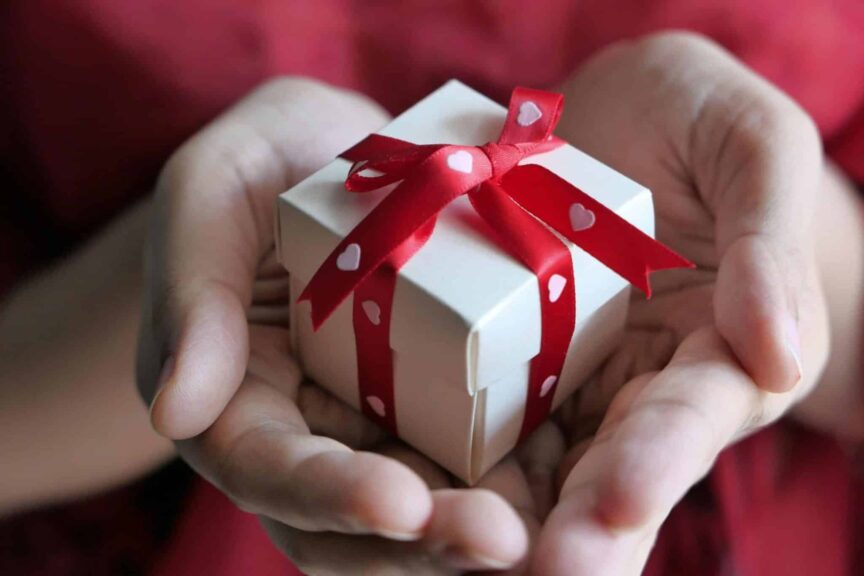 A heartfelt moment captured with hands holding a small gift box tied with a red ribbon, pebbling, friendships