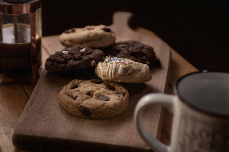 Delicious assorted cookies on a wooden board accompanied by coffee, perfect for a cozy snack time.