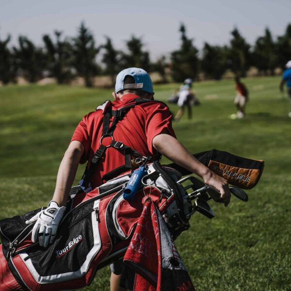 A golfer in red carrying a bag on a lush green golf course during a sunny day./VR headsets