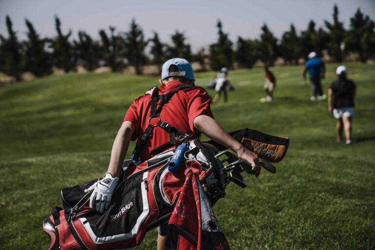 A golfer in red carrying a bag on a lush green golf course during a sunny day./VR headsets