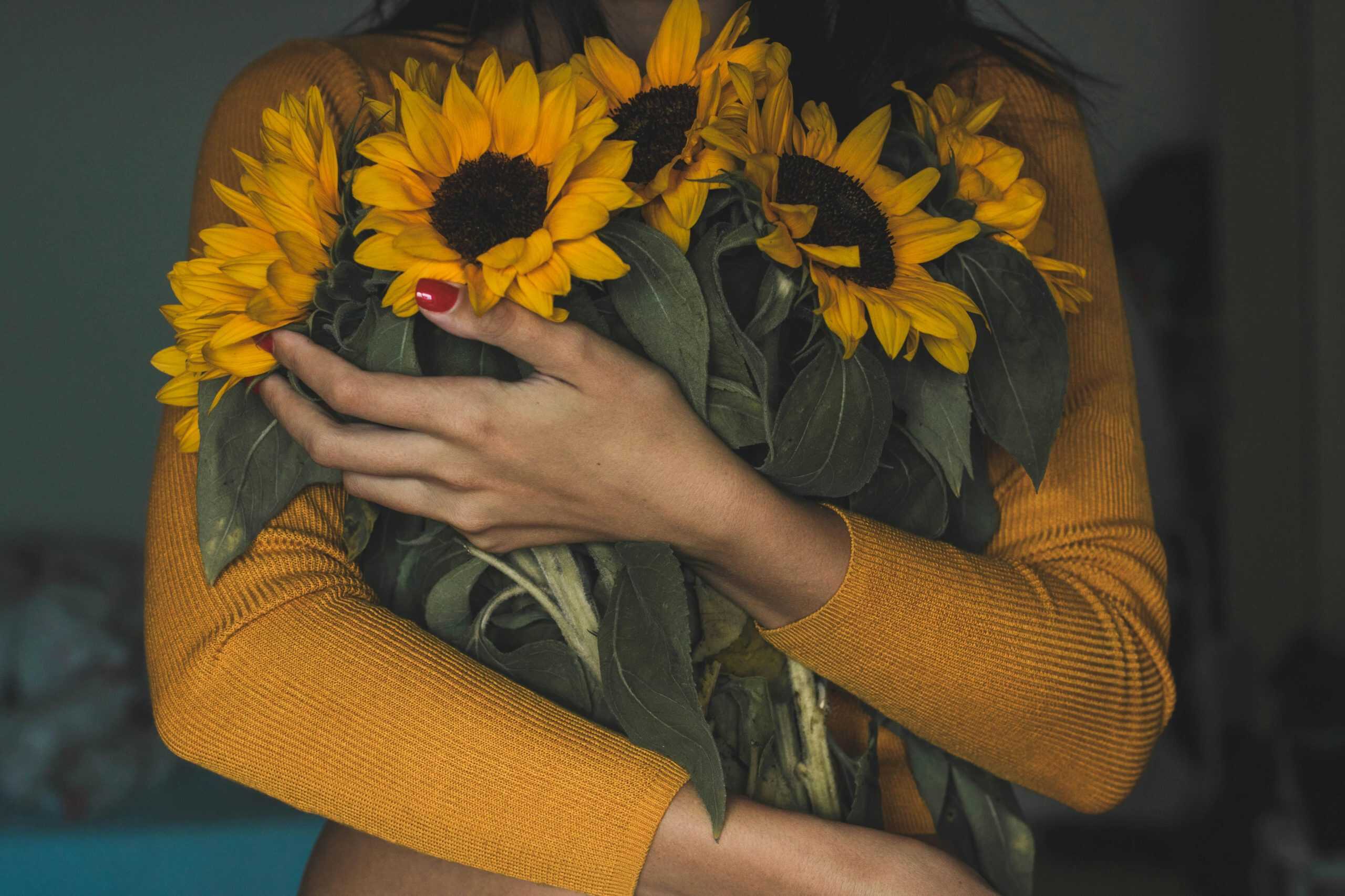 A woman in a mustard sweater holding a bouquet of sunflowers, exuding a warm and cozy vibe.