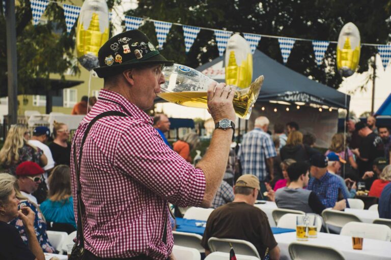 Oktoberfest, West Central Florida, Man enjoying a large beer mug at an Oktoberfest celebration outdoors with a lively crowd.