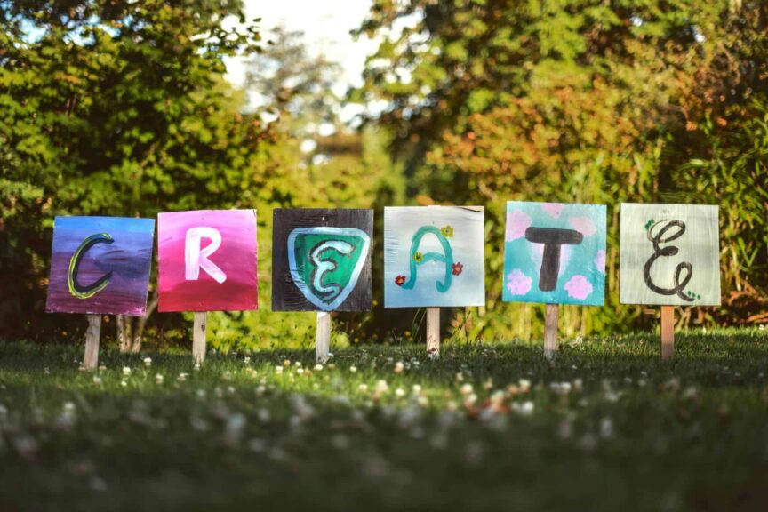 Vibrant painted signs spelling 'CREATE' in a lush outdoor garden setting. creative genius venus in leo