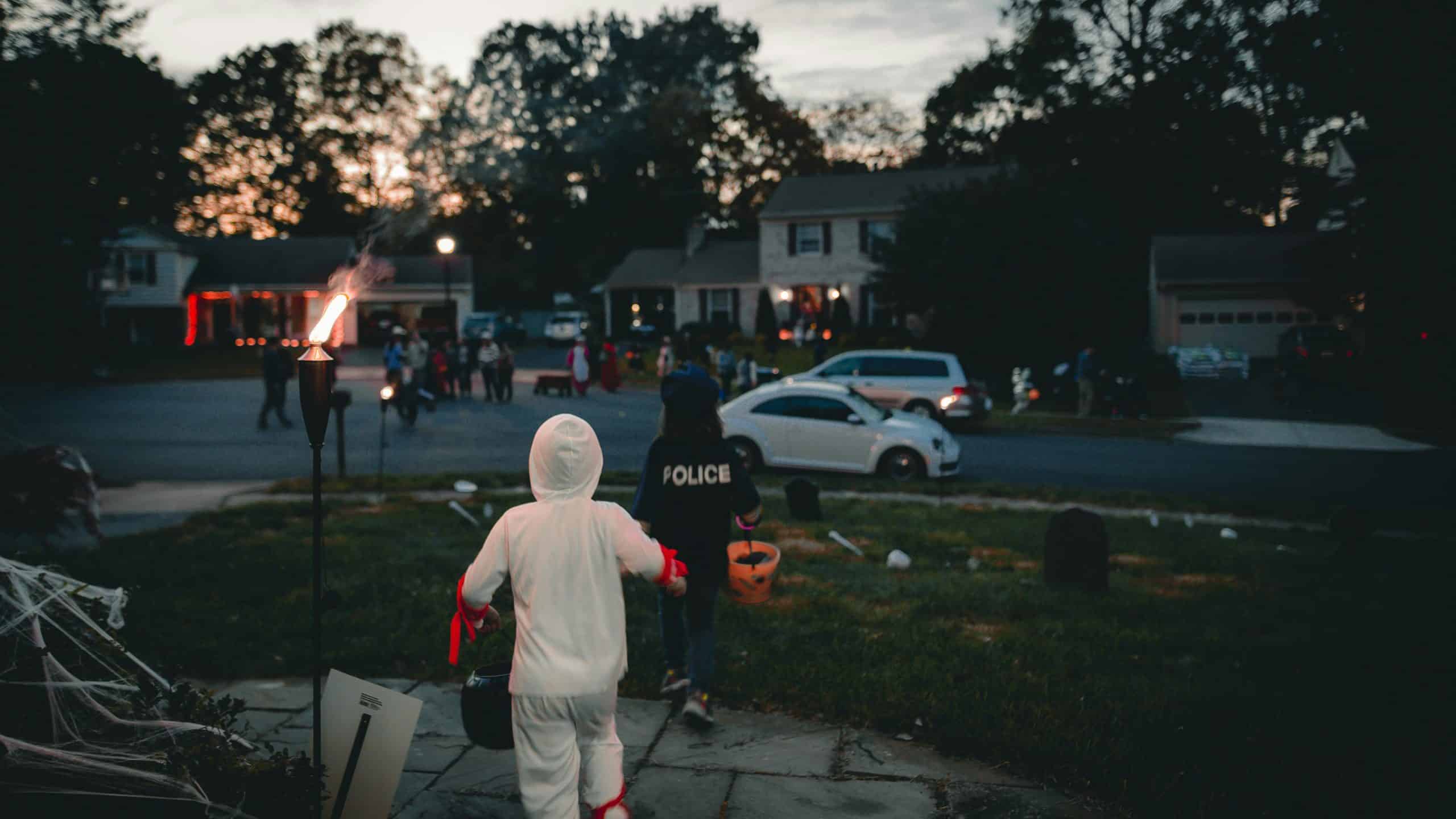 Children dressed in Halloween costumes trick-or-treating in a neighborhood at dusk, celebrating the festive spirit.