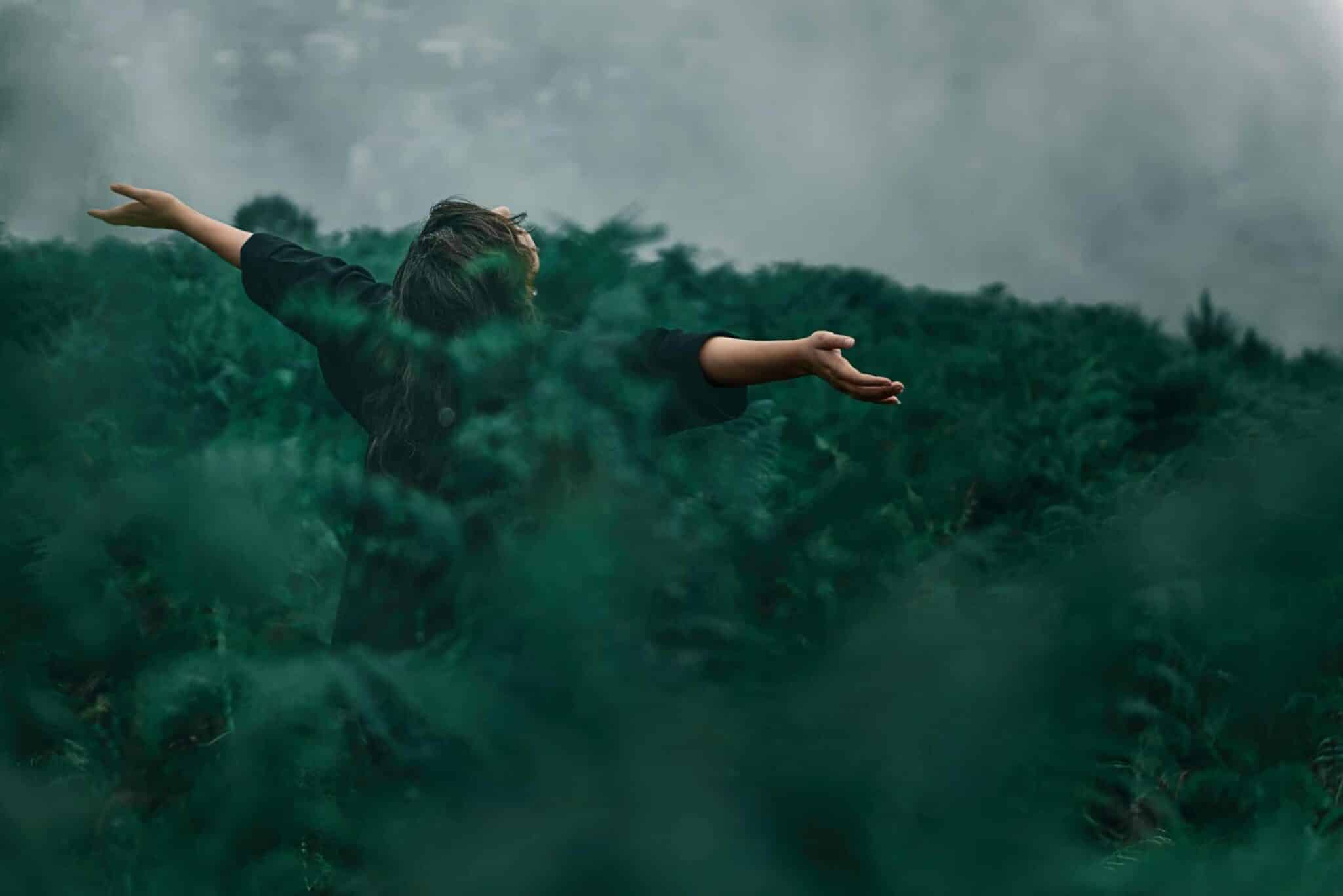 A woman with open arms enjoying freedom in a foggy green landscape. nature
