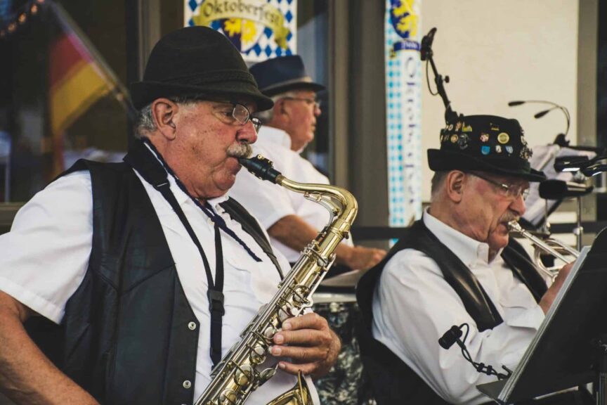 Elderly musicians perform with saxophone and trumpet at an Oktoberfest festival outdoors.