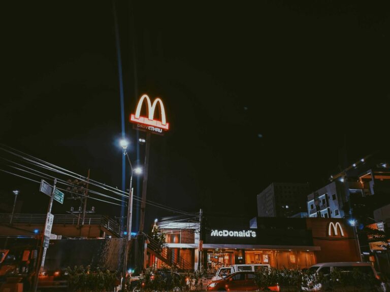 A brightly lit McDonald's restaurant in a city setting during nighttime, showcasing neon signage.