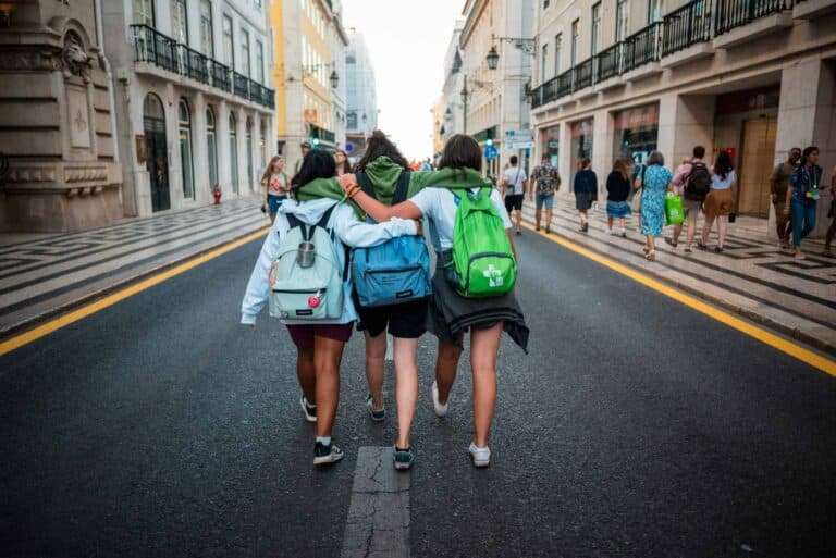 Three young friends walk arm-in-arm on a Lisbon street, showcasing friendship and travel spirit.
