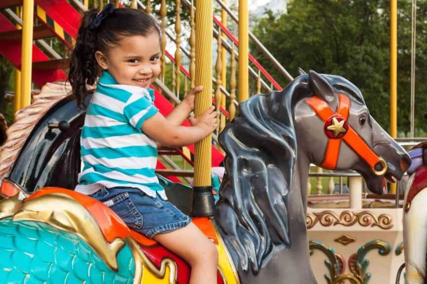 Joyful child enjoying a carousel ride in a vibrant amusement park setting. Theme parks