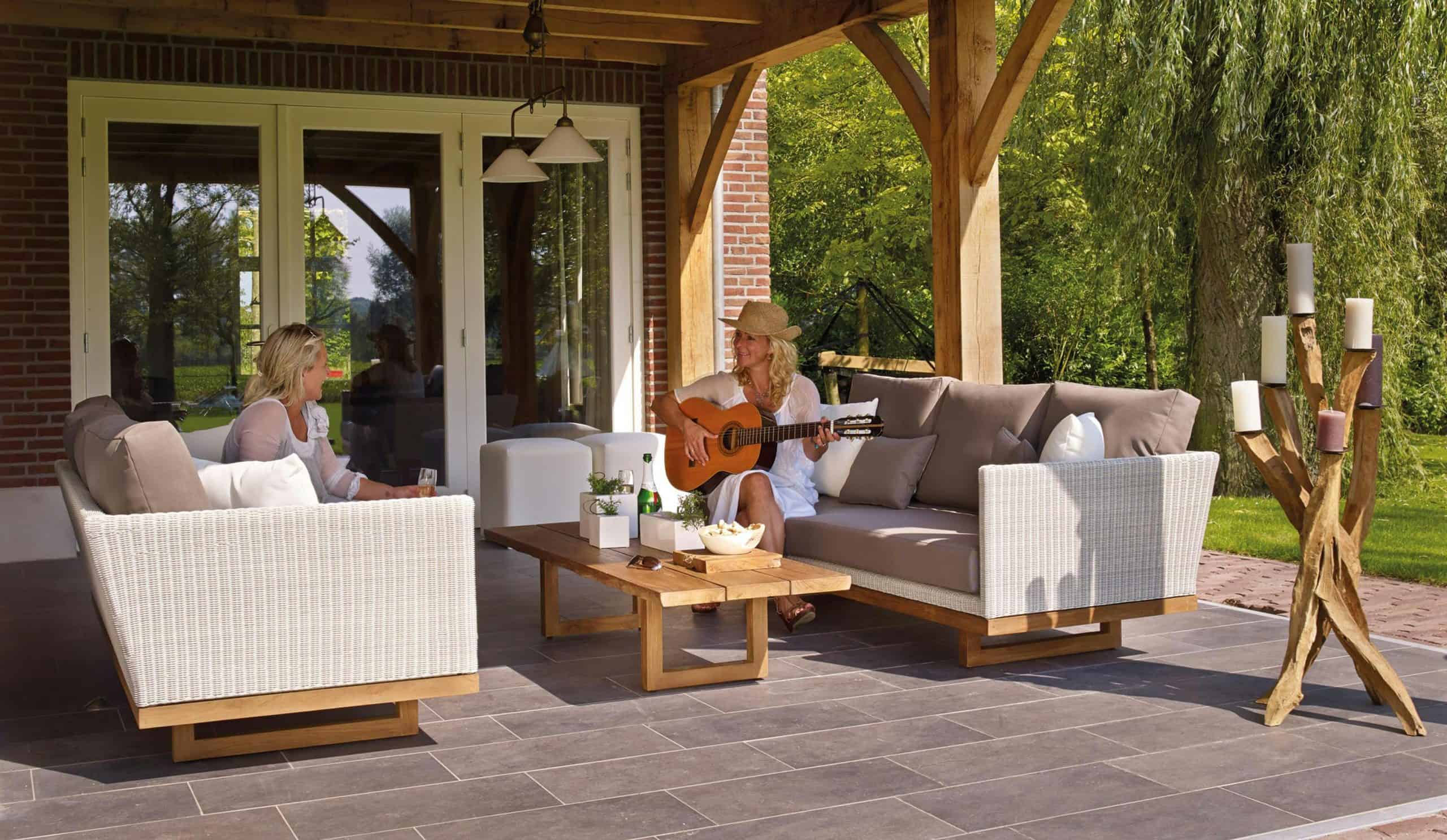 Two women enjoying a serene patio scene with a guitar and candles, surrounded by greenery, backyard lounge