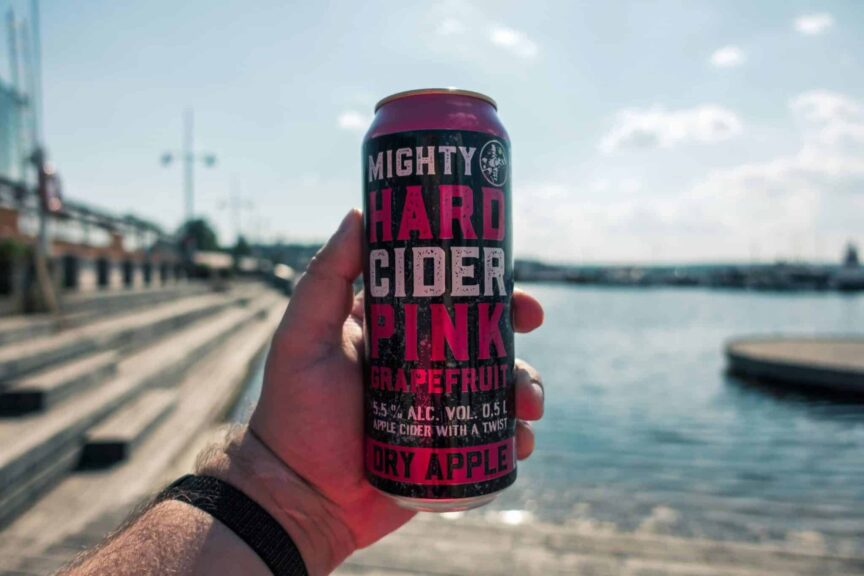 Person holding a grapefruit hard cider can near a scenic waterfront in Lahti, Finland, enjoying a refreshing fall drink outdoors.
