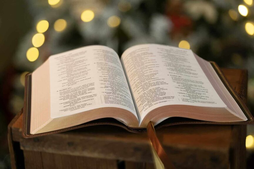 Open Bible resting on wooden surface with blurred festive background lights, daily devotion