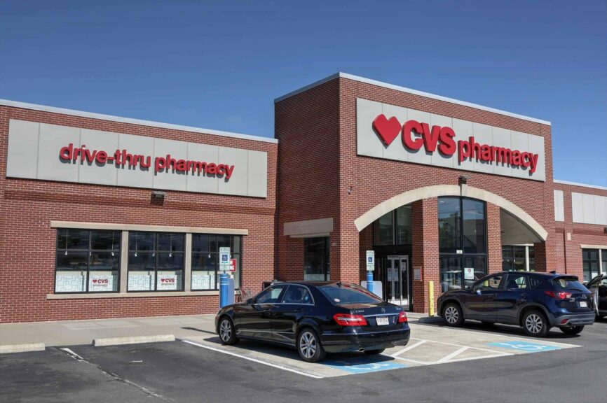 CVS Pharmacy storefront with drive-thru and parked cars, illustrating the CVS recall involving baby drops, colon cleanser, and ice cream products.
