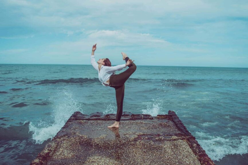 A person practices a high-level yoga pose on a pier by the ocean, capturing serene balance.