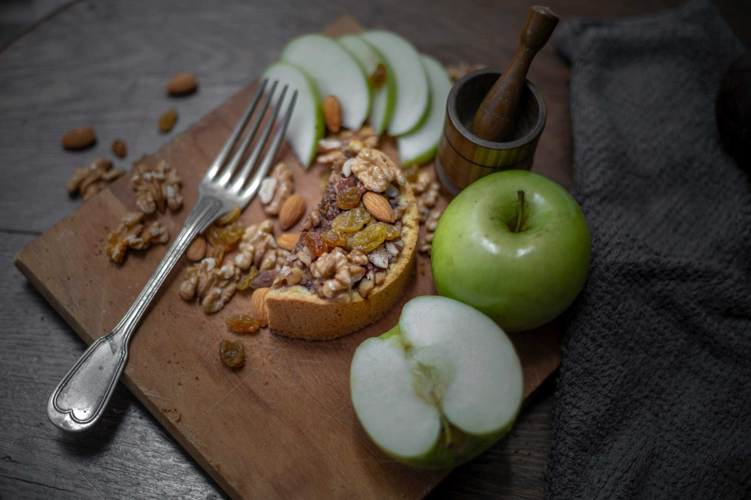A delicious rustic tart with walnuts, raisins, and fresh green apples on a wooden board.