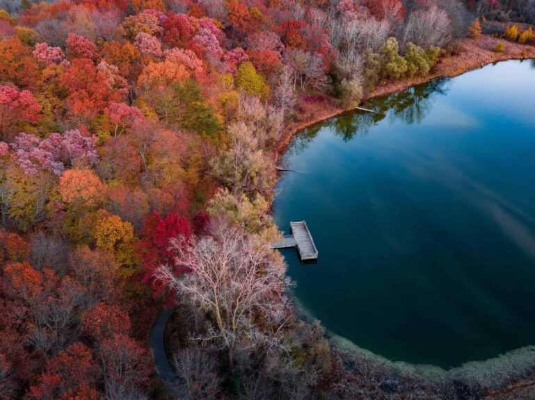 Midwest road trip Aerial view of vibrant autumn colors surrounding a serene lake in Holly, Michigan.