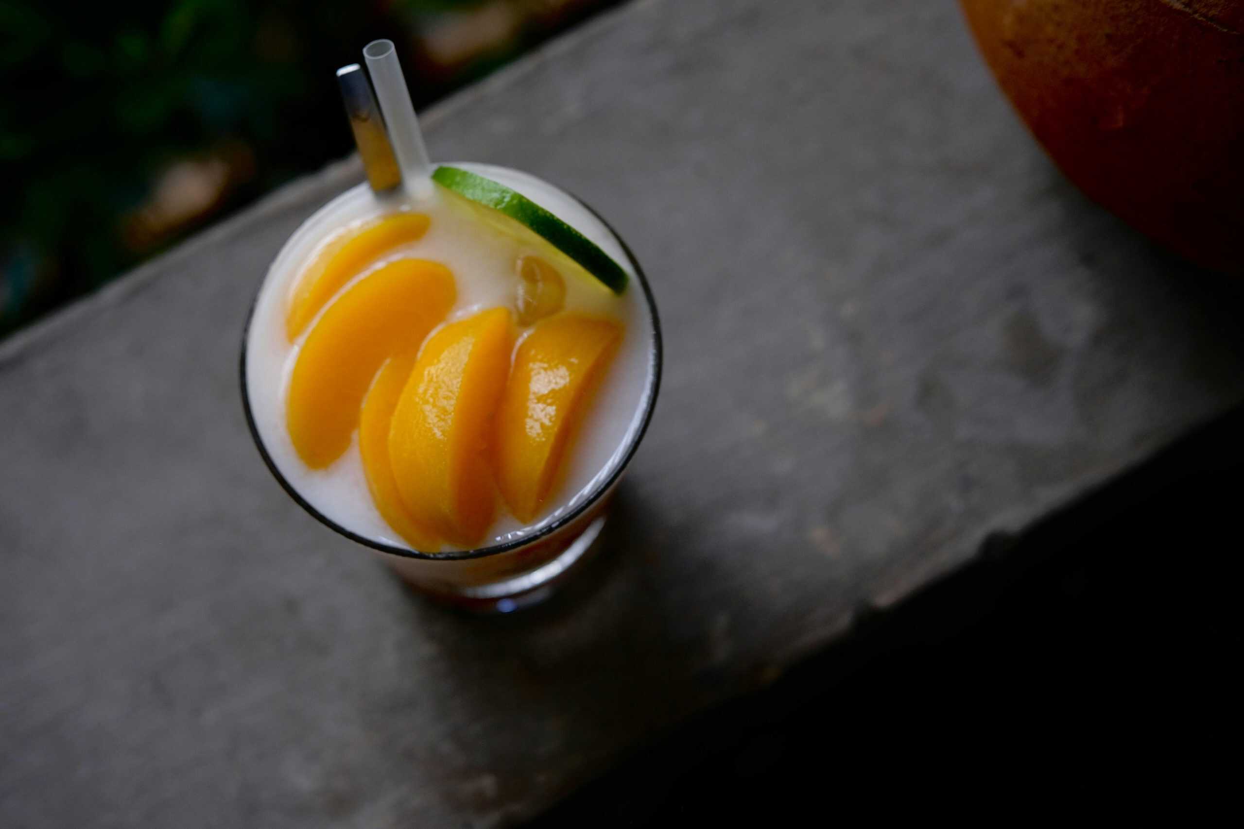 Top-down view of a refreshing peach and lime cocktail with straws on a rustic surface.