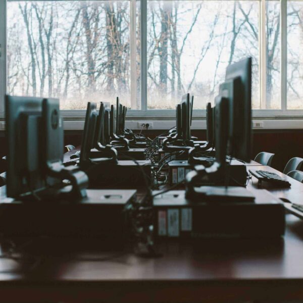 An empty computer lab with multiple workstations and large windows during the daytime. pc/intel