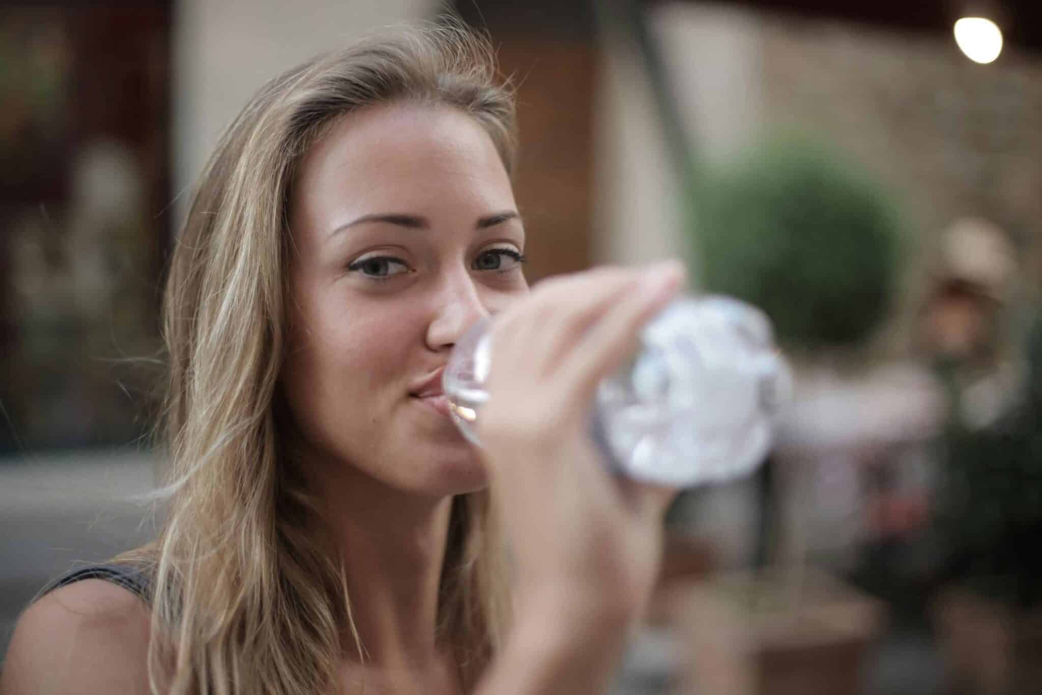 Portrait of a smiling woman drinking bottled water outdoors, enjoying hydration and relaxation. electrolytes