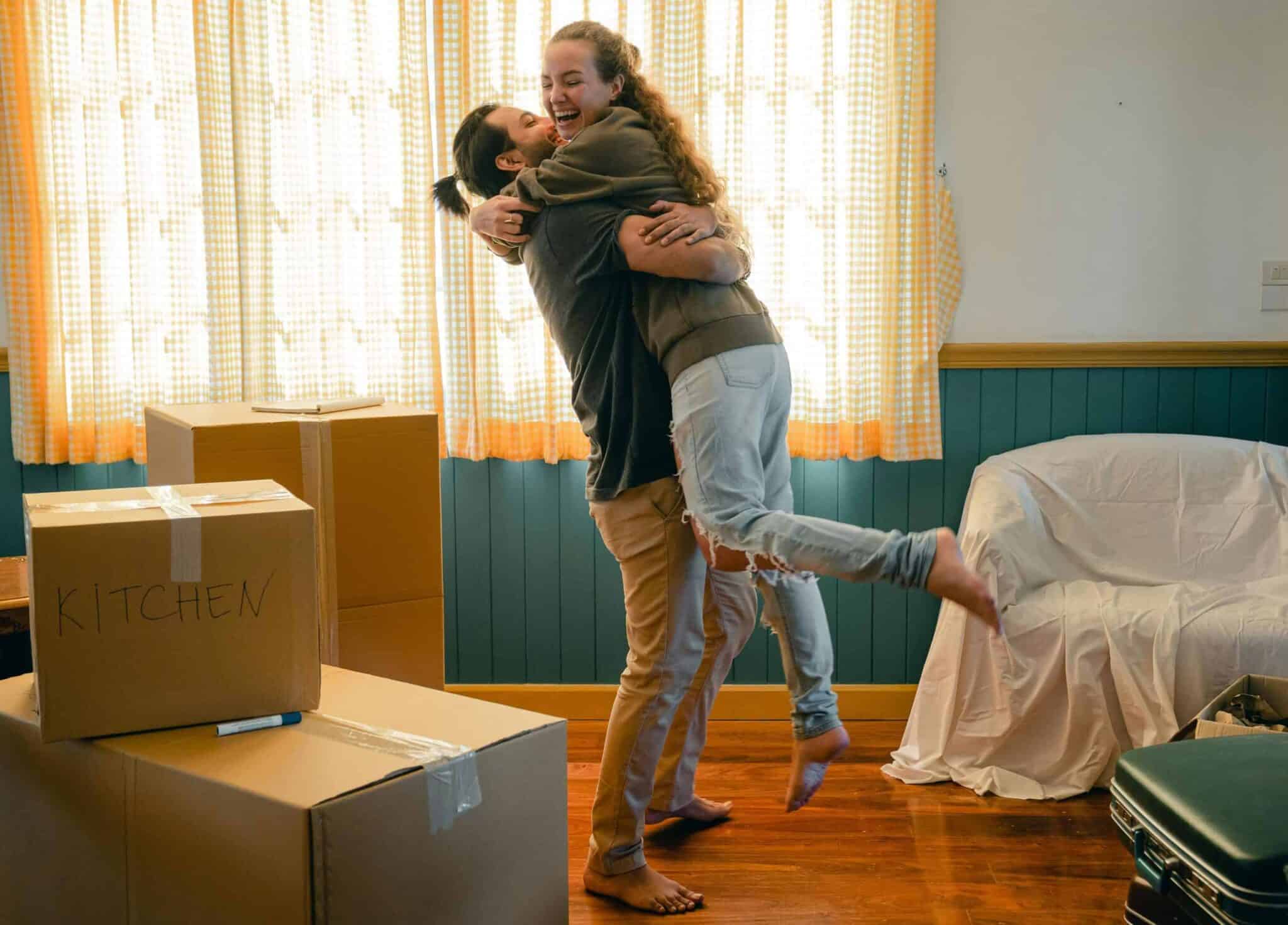 This photograph features a happy couple in an apartment with boxes. Micro-ceremonies can help create positive experiences for people living together.