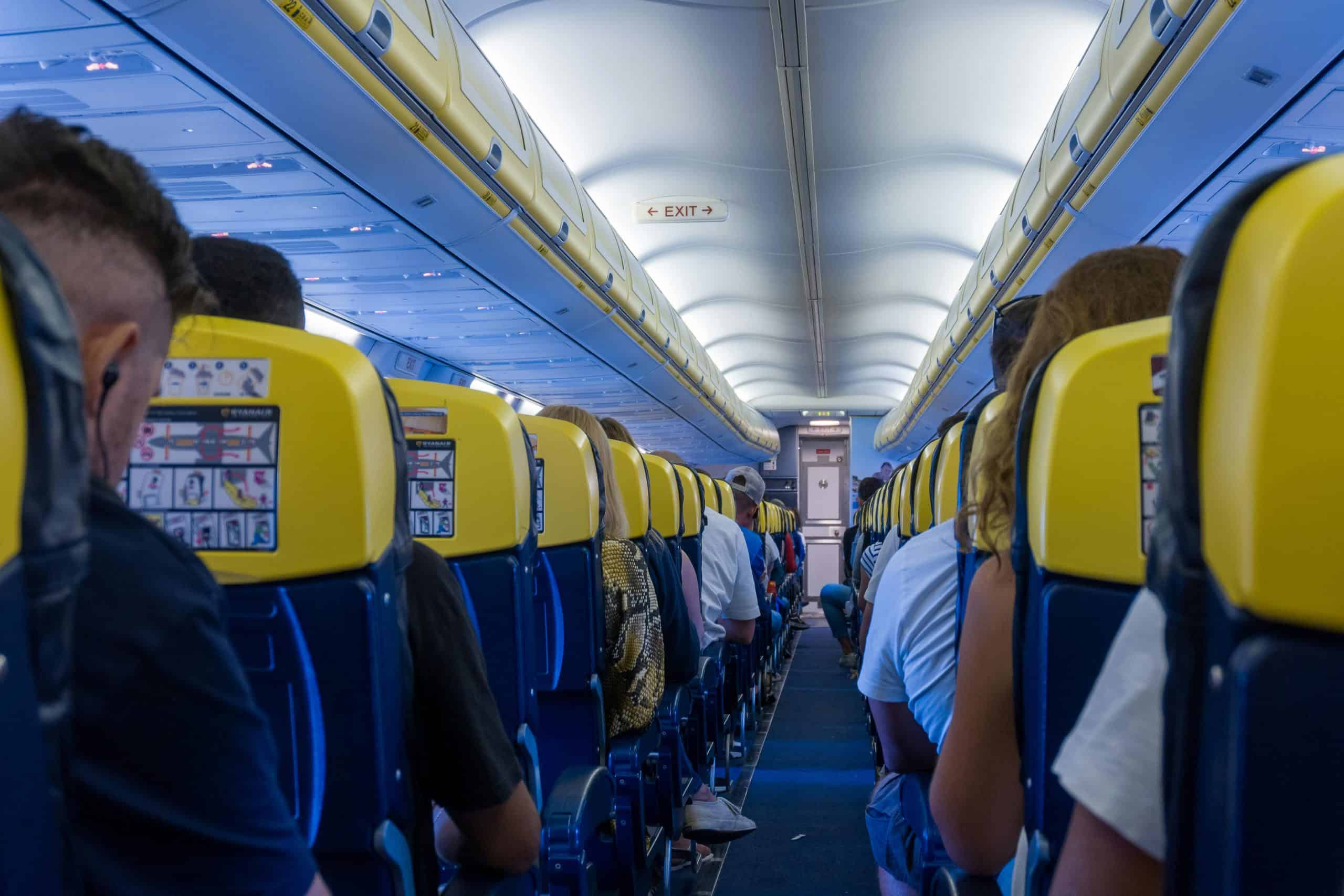 View of passengers seated inside an airplane cabin with yellow seatbacks and overhead bins.