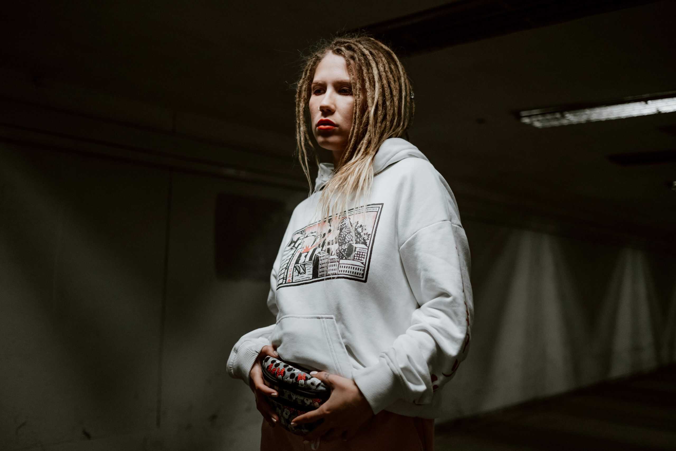Stylish woman with dreadlocks wearing a white hoodie in a moody urban setting.