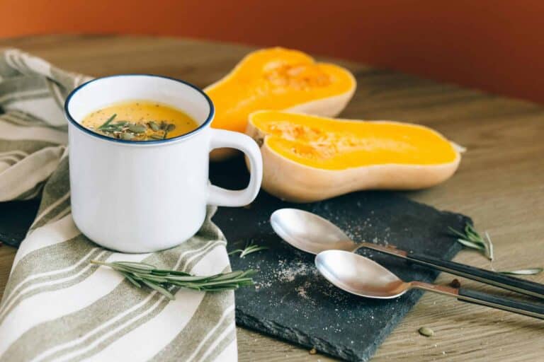 A cozy setting with butternut squash soup in a mug, complemented by fresh ingredients and rustic decor. pumpkin