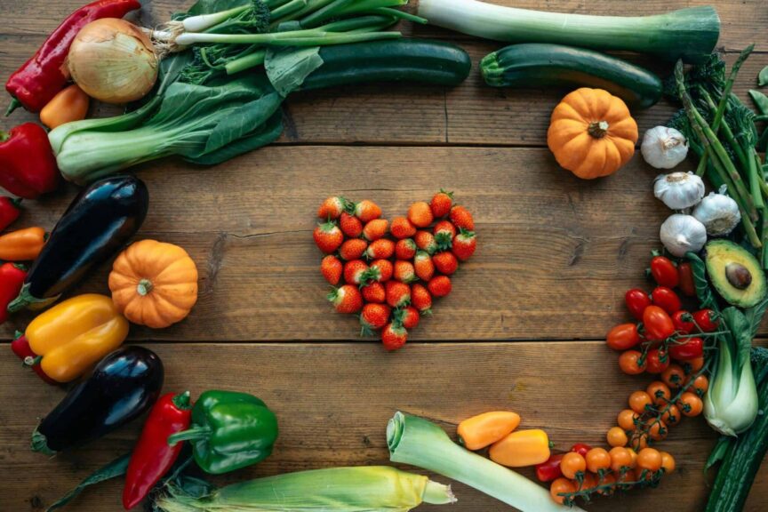 in-season, Vibrant fruits and vegetables arranged heart-shaped on a wooden surface, top view.