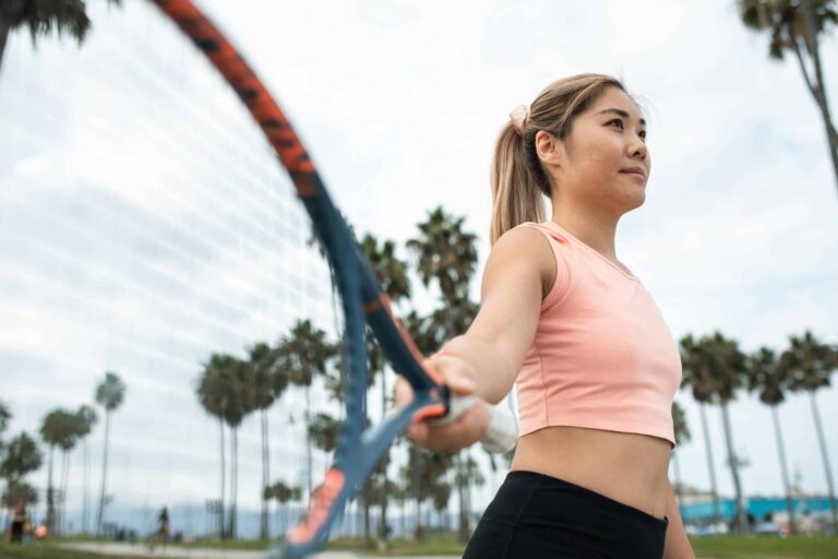 Active woman playing tennis in park with palm trees surrounding tenniscore