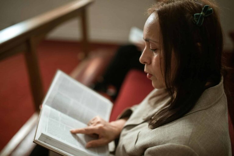 A woman in a church pew reading a Bible, showing devotion and faith, women, lessons