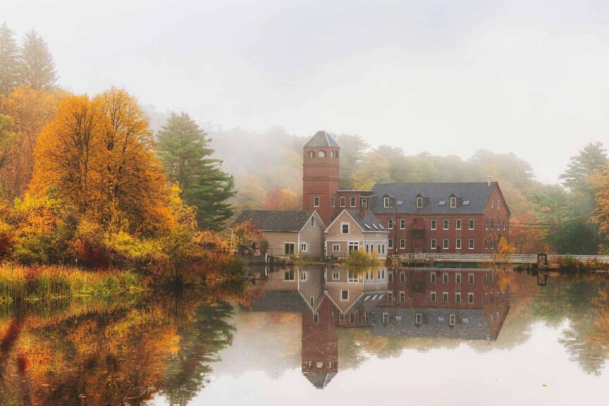 Road trip, Northeast, Serene autumn scene with a historic mansion and vibrant foliage reflected on still water.