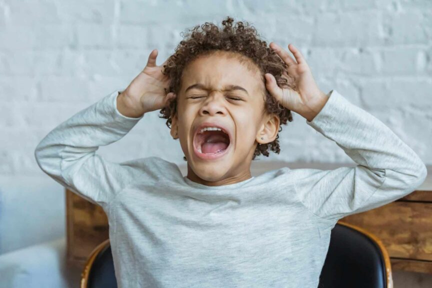 Young boy showing frustration indoors with hands on head, eyes closed, mouth open, spoiled child. parenting