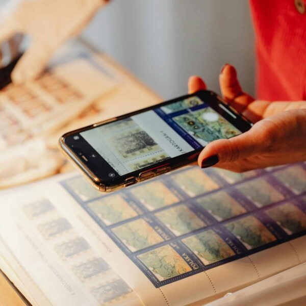 Individual photographing a stamp collection using a smartphone for cataloging. Internet archive
