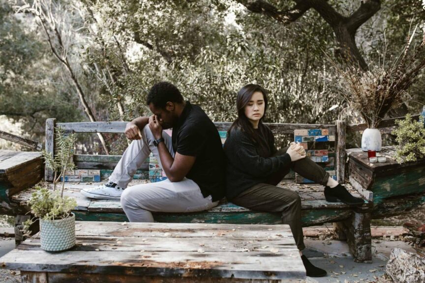 Infidelity, cheating, A couple sits back to back on a wooden bench, indicating a disagreement or breakup.