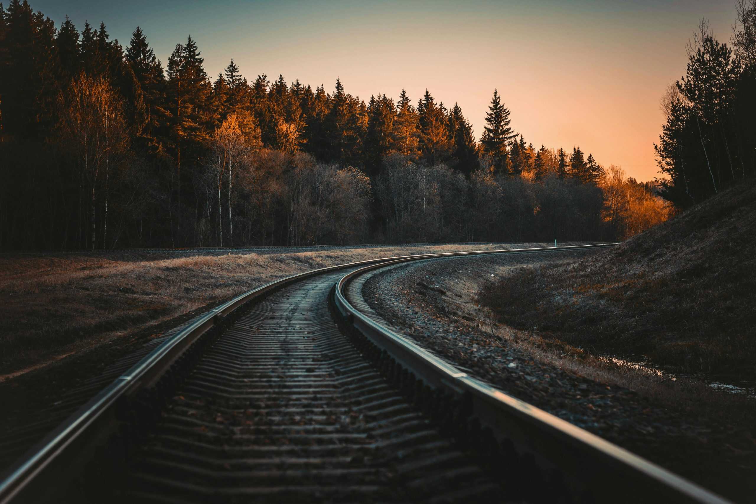 A serene view of a railway track in a forest at sunset with Autumn colors.