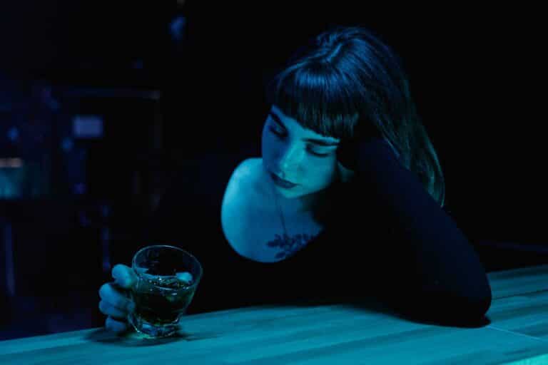A woman with eyes closed holds a drink at a dim bar. Moody nightlife scene. nonalcoholic drinks