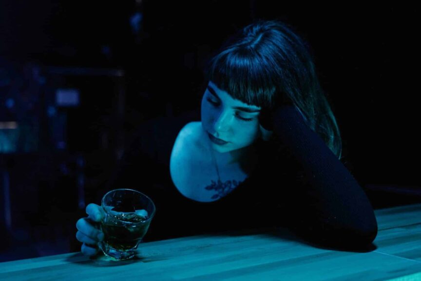A woman with eyes closed holds a drink at a dim bar. Moody nightlife scene. nonalcoholic drinks