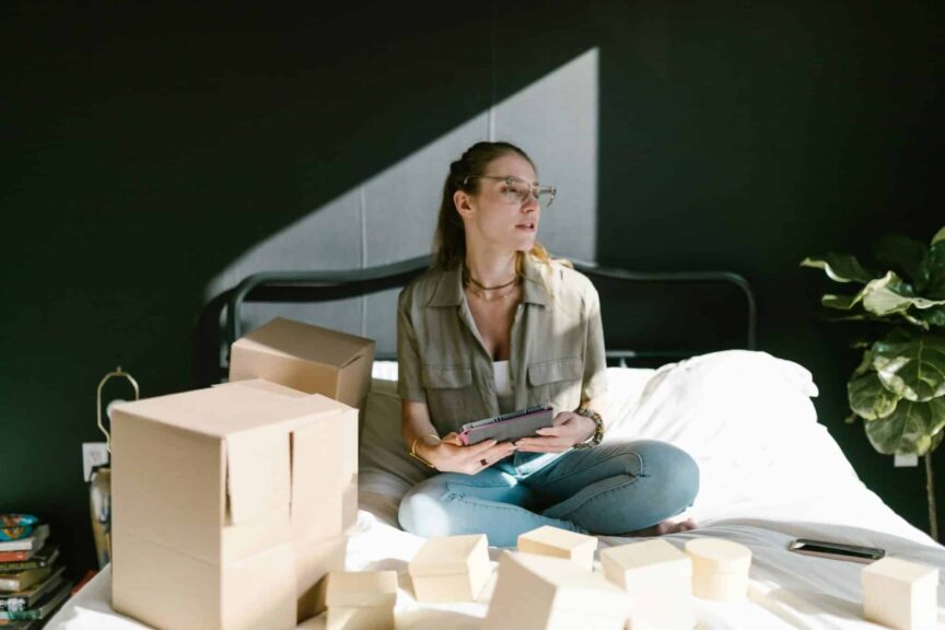 Side hustle, Woman working on e-commerce startup with tablet and boxes on bed.