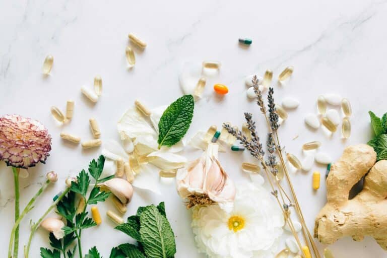 A flatlay of natural herbs, supplements, and flowers on a marble background. creatine