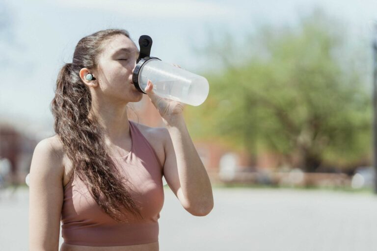 Young woman in sportswear drinks water outdoors, enjoying a sunny day, electrolyte, heat waves