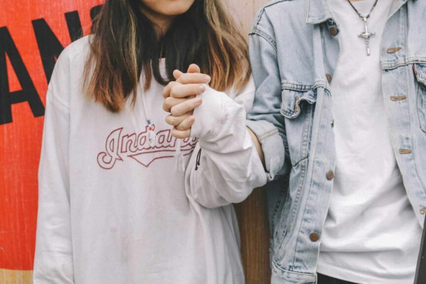 Young couple holding hands in casual attire, symbolizing love and togetherness.