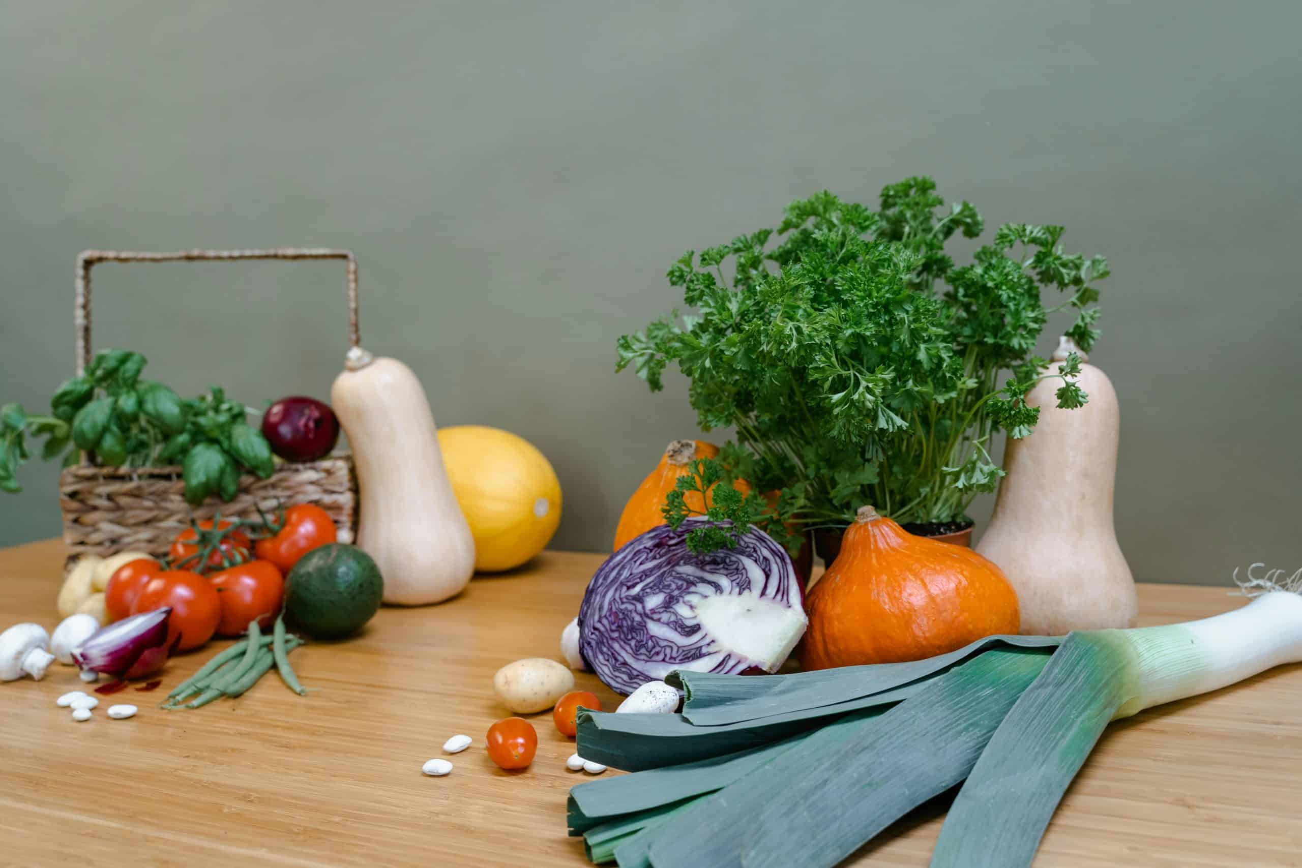 A diverse assortment of fresh vegetables including squash, tomatoes, and greens on a wooden table.