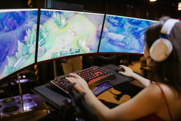 A young woman intently gaming on a multi-screen setup, showcasing vibrant gaming visuals./adult-themed games