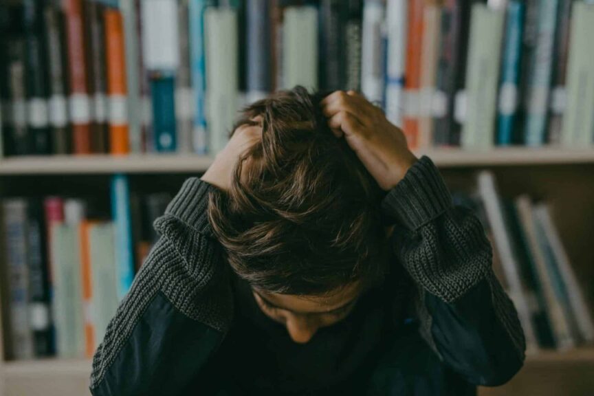 head Lice, children, kids hair, A child appears stressed and frustrated while seated in a library, holding their head.