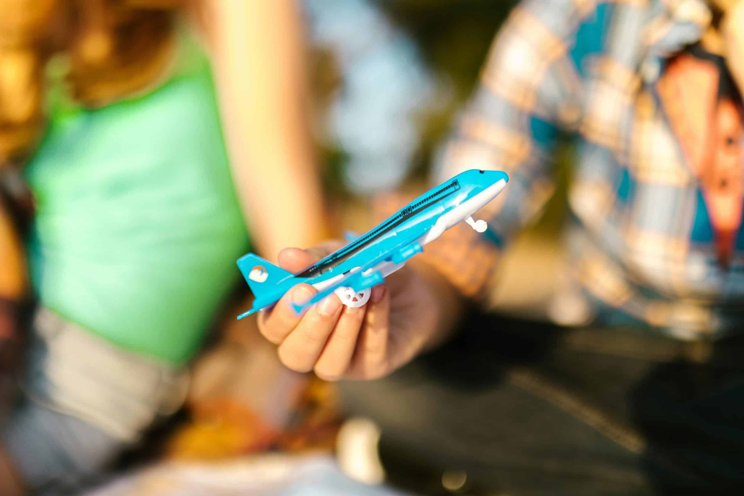 Close-up of a child playing with a blue toy airplane outdoors during the day.